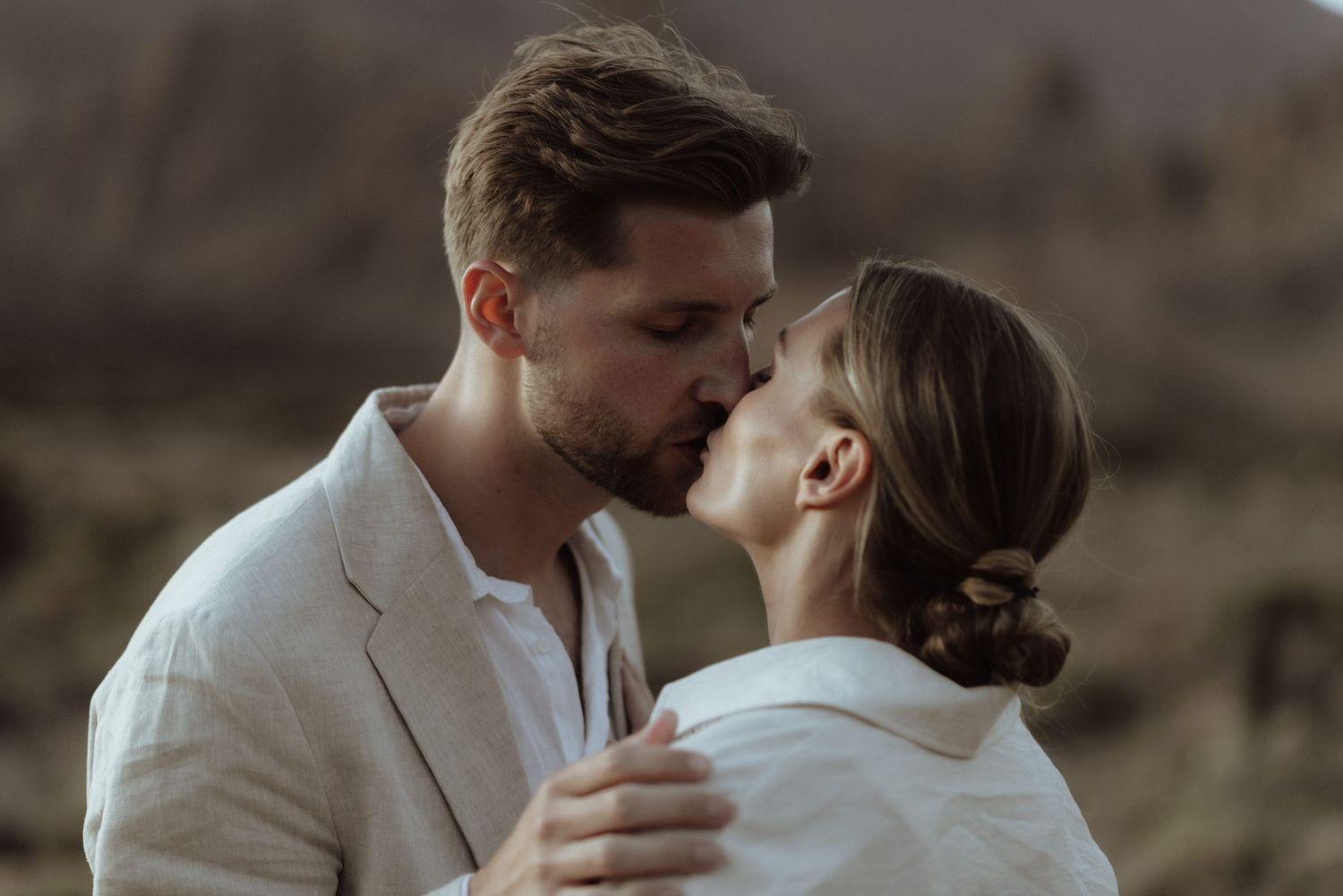 Intimate couple in matching white outfits embrace closely during a desert photoshoot.