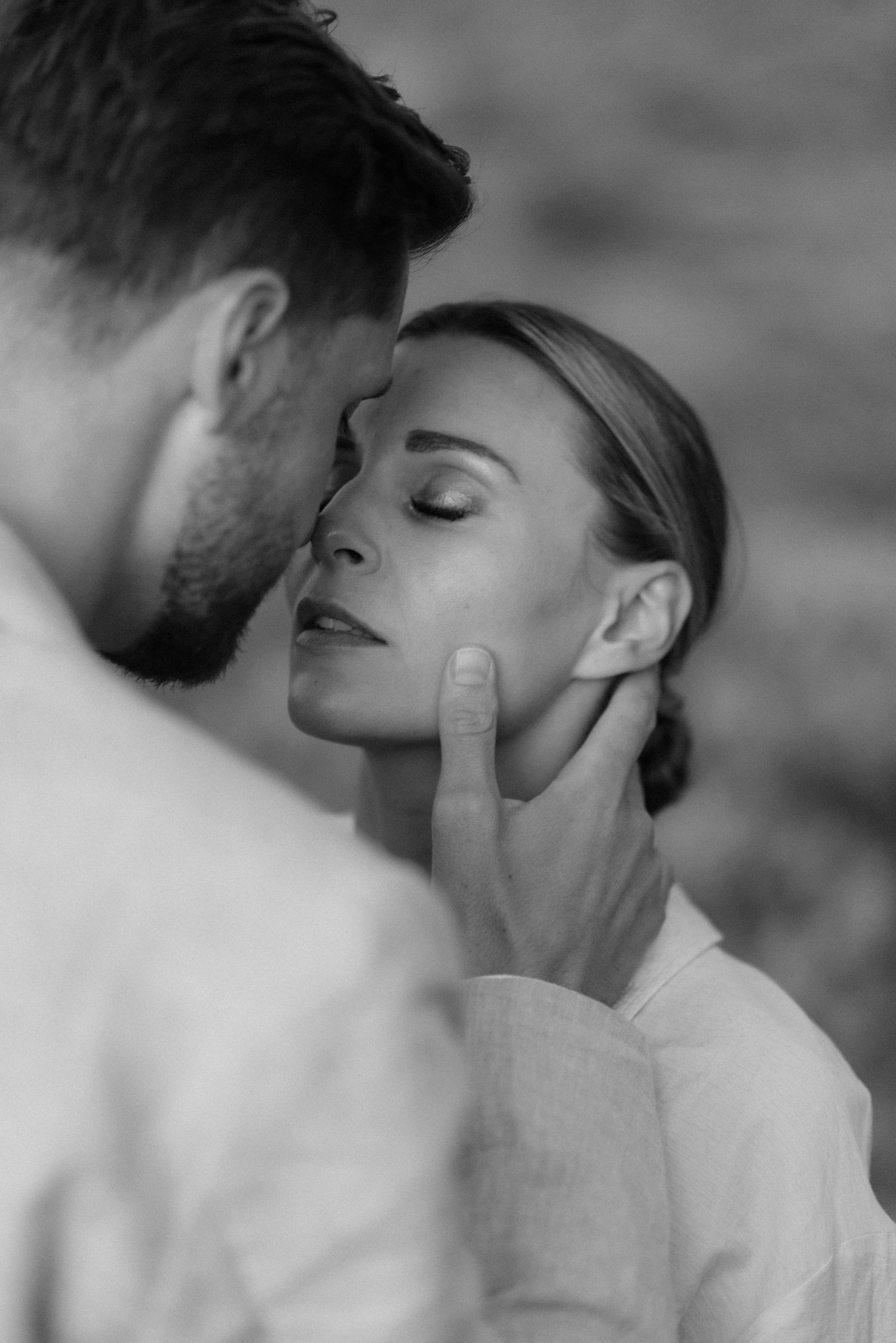 A tender intimate black and white portrait capturing a romantic moment between a couple in soft lighting.