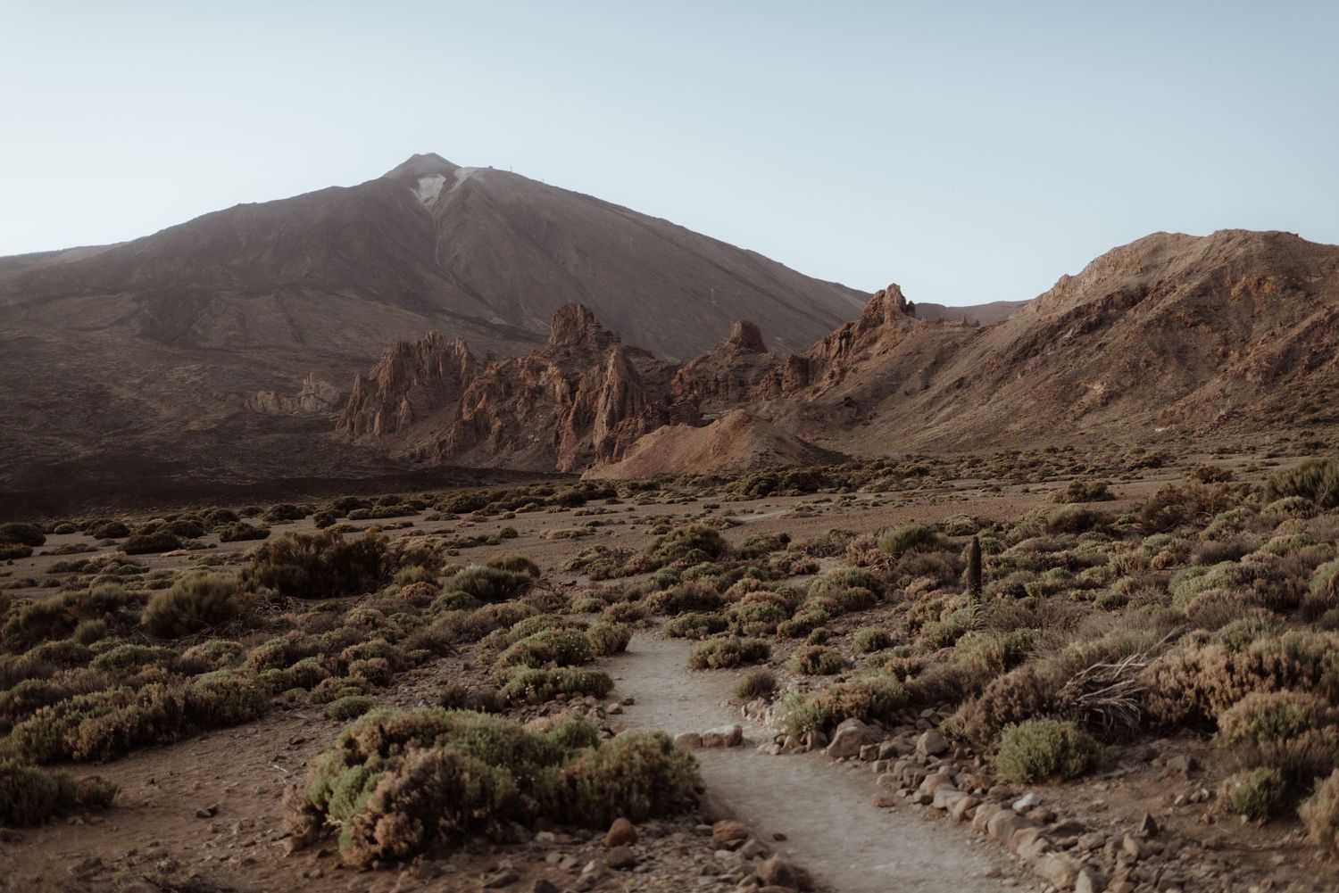 A winding dirt path leads through desert terrain towards a majestic mountain peak.