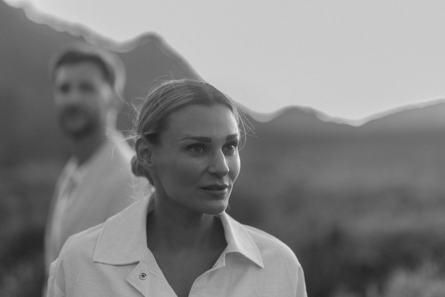 A soft black and white portrait with mountains visible in the distant background.