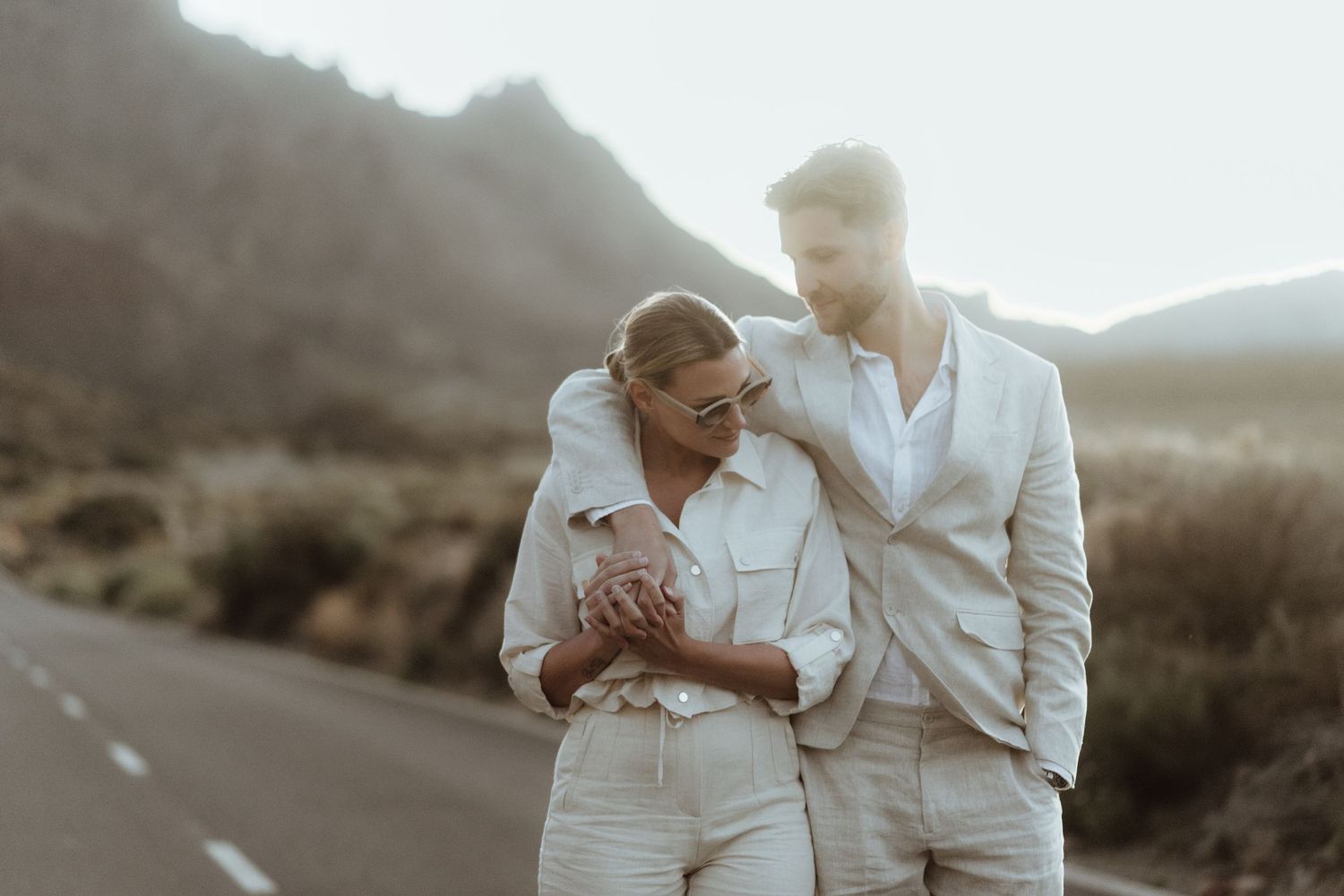 A couple in matching white outfits sharing an intimate moment on a desert road.