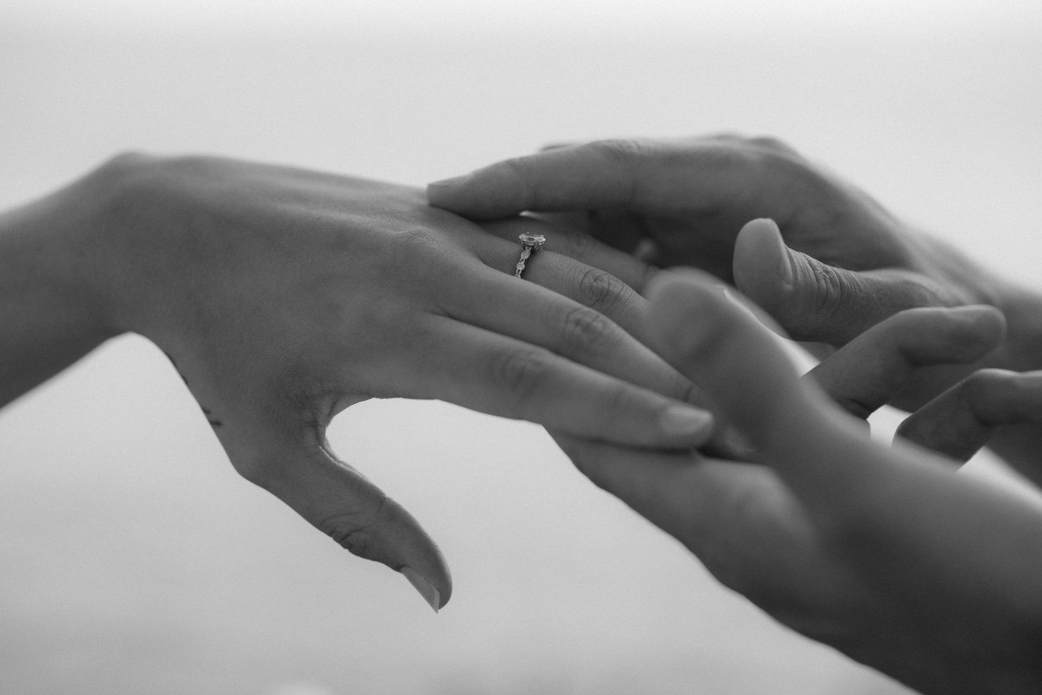 Close-up black and white photo of hands exchanging rings in an intimate moment.