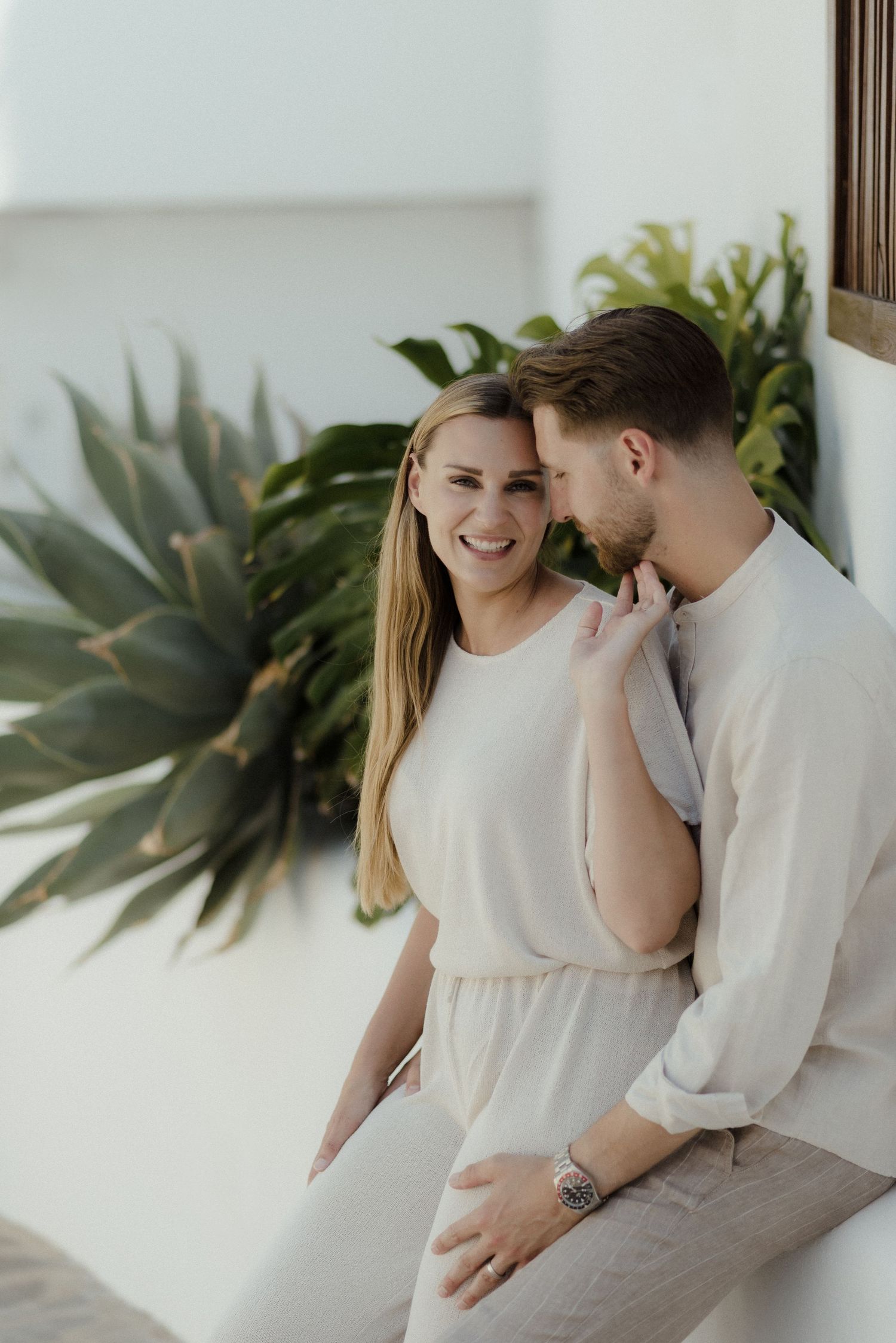 A romantic couple sharing an intimate moment on a patio with tropical plants in the background.