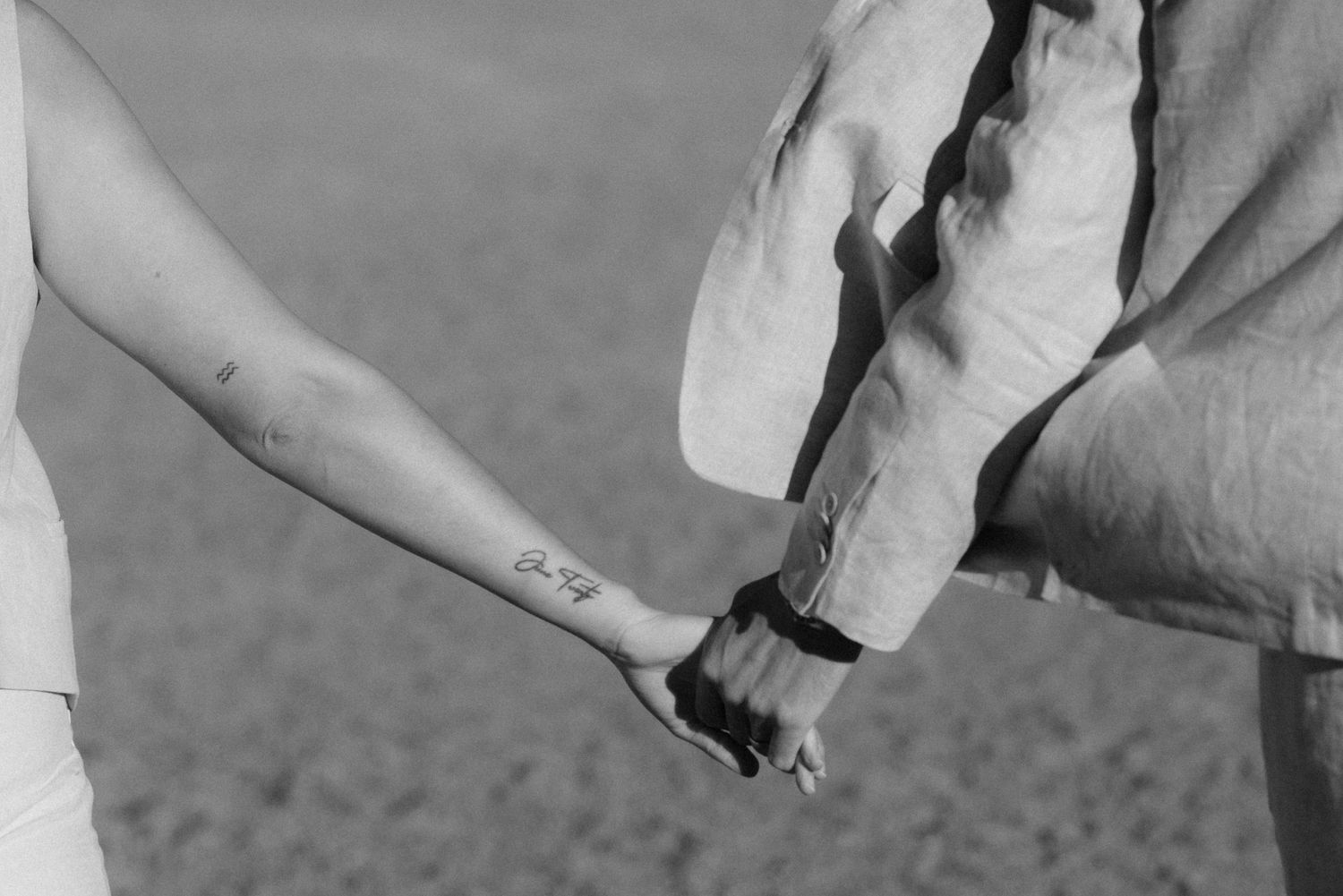 Close up black and white photo showing person's finger touching small tattoo on another person's arm.