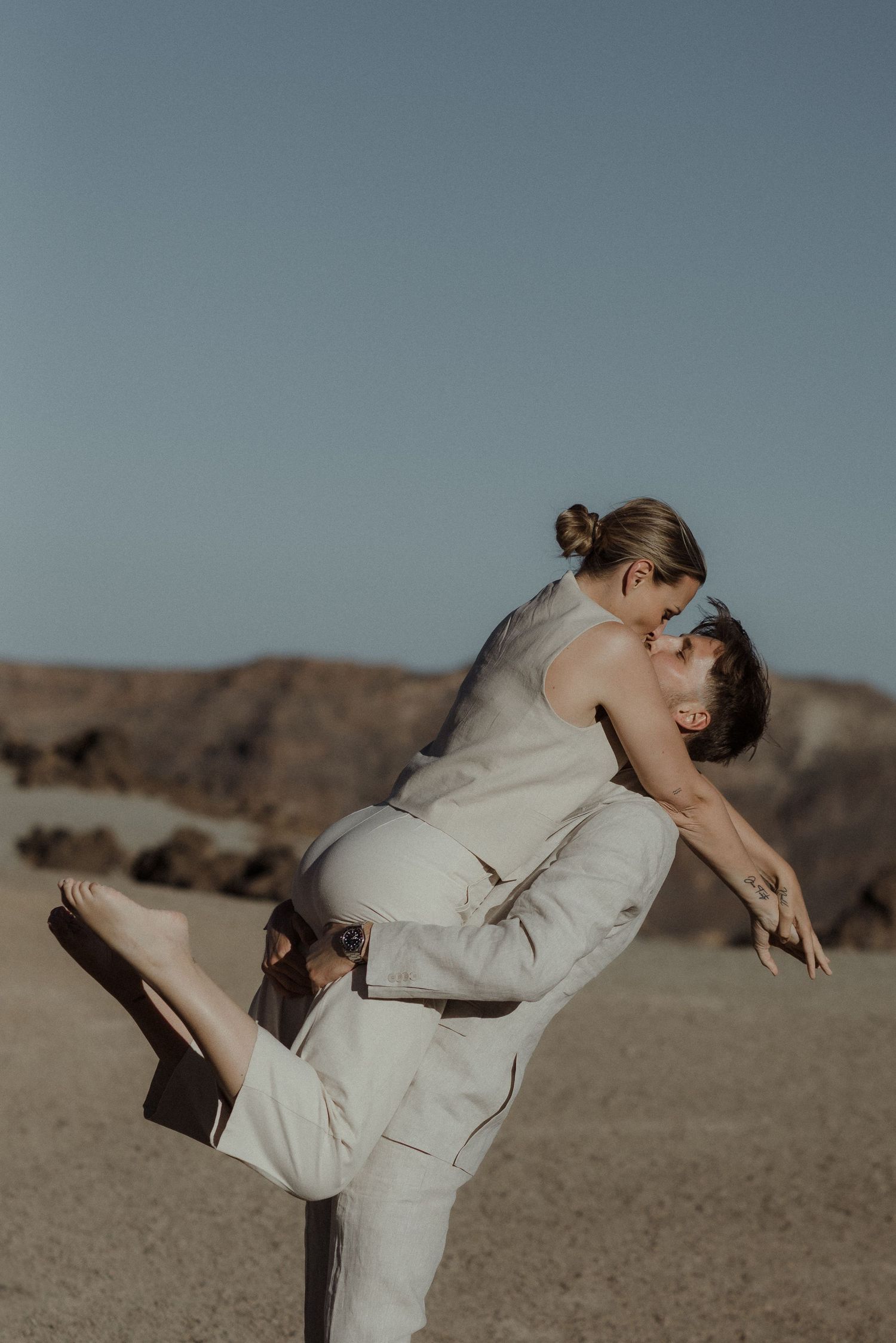 Dancing figure in flowing white dress poses gracefully against desert landscape backdrop.