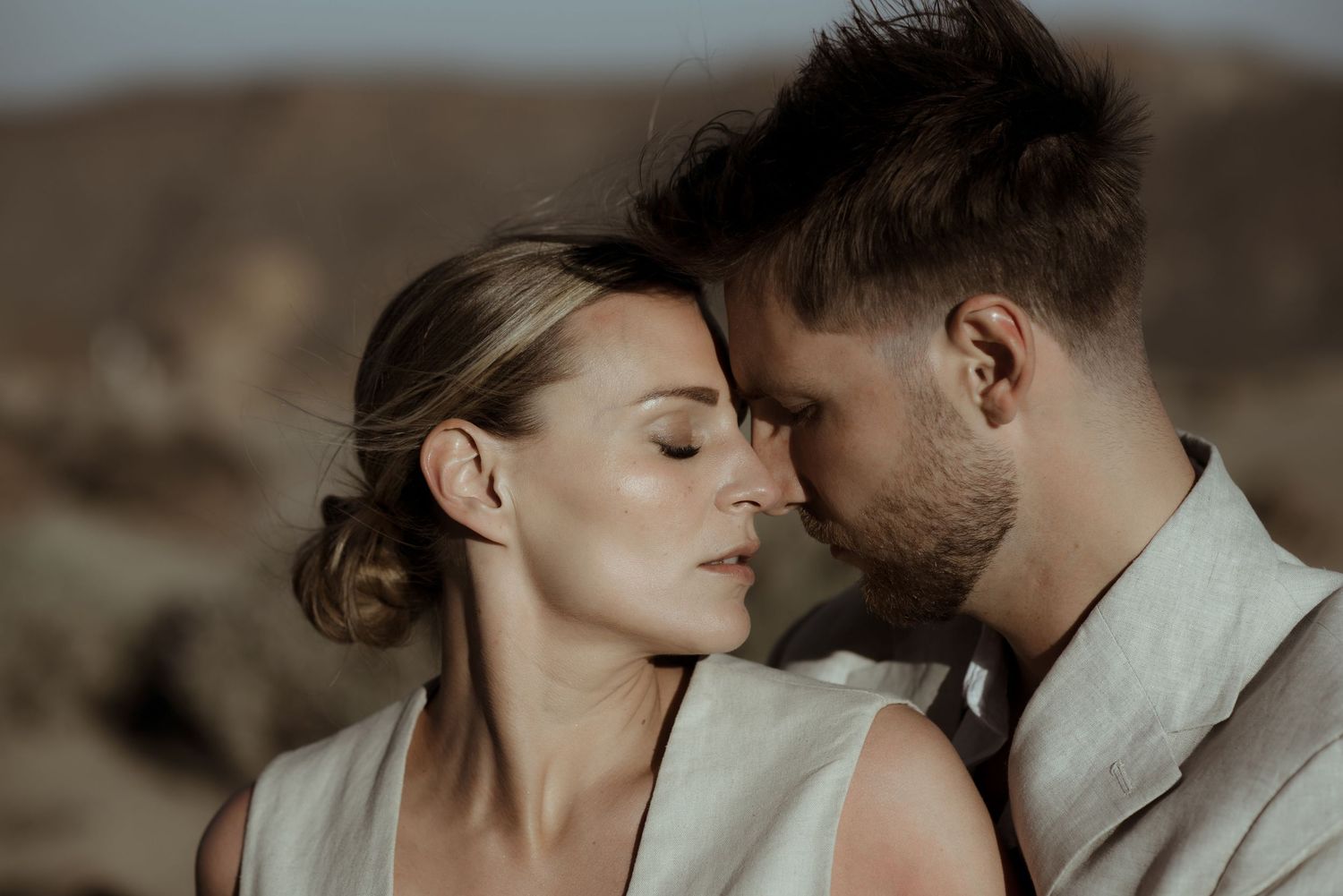 Intimate portraits of couple sharing tender moments against desert mountain scenery in neutral tones.