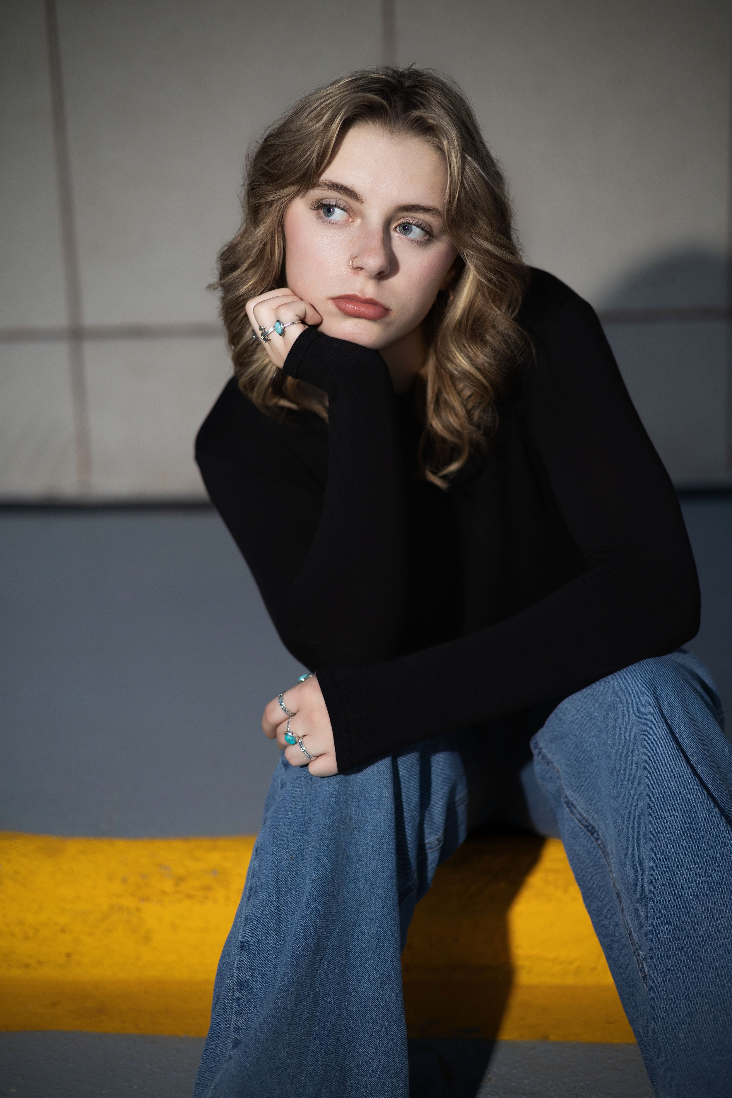 Fashion portrait of woman in black sweater and jeans posing expressively against minimalist studio background.