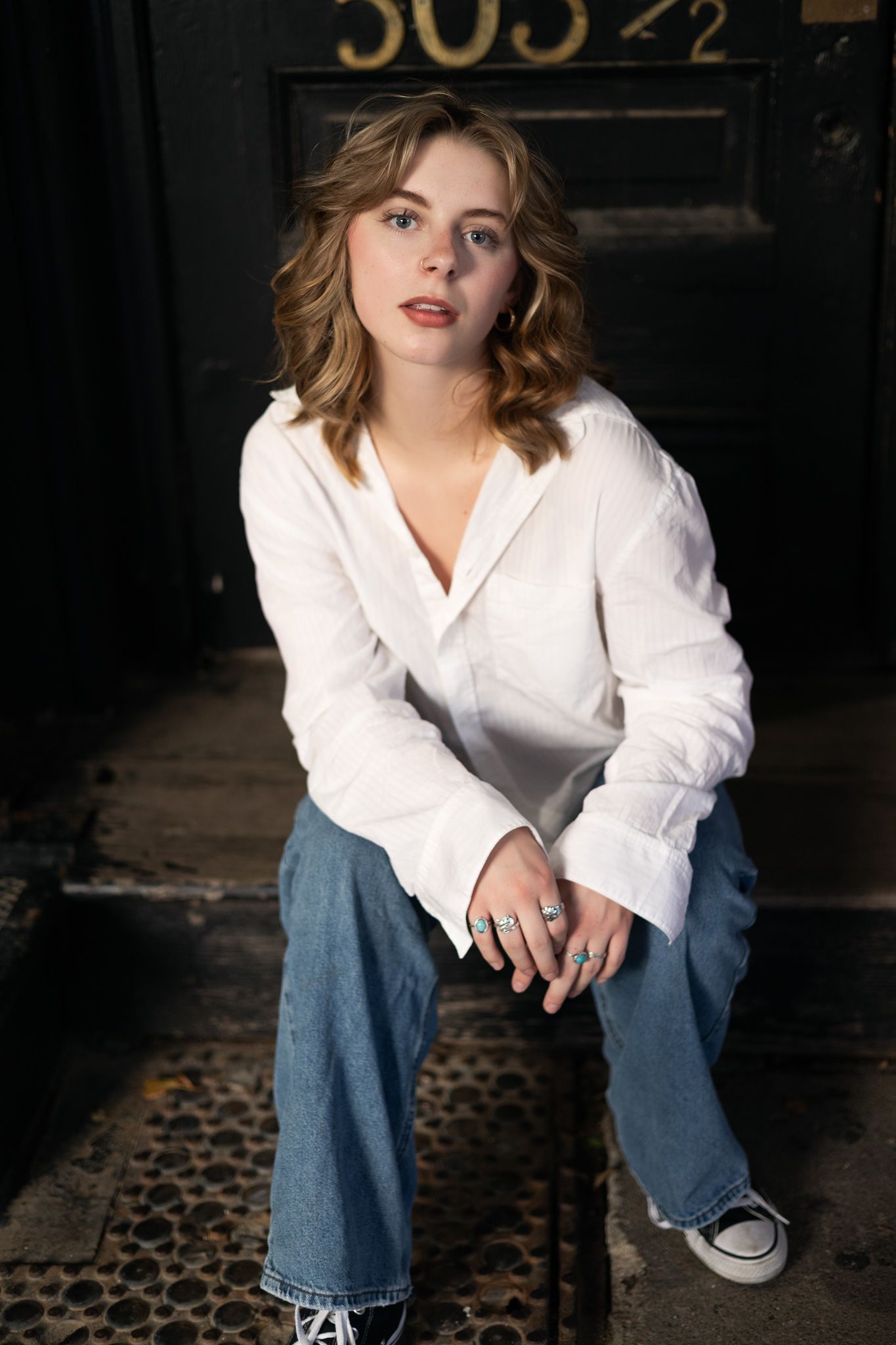 A fashion portrait of someone wearing a white button-down shirt and relaxed blue jeans in a dark moody setting.