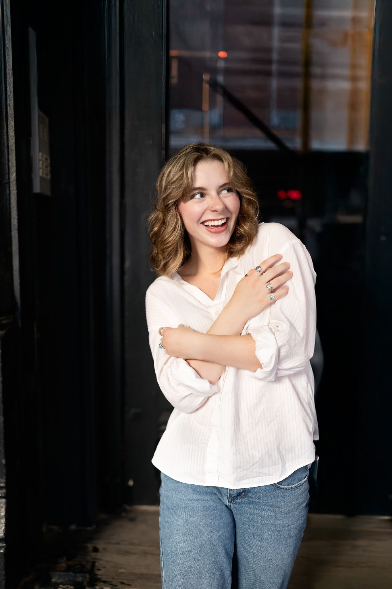 A person wearing a white button-down shirt and jeans poses playfully against a dark background in a photo series.