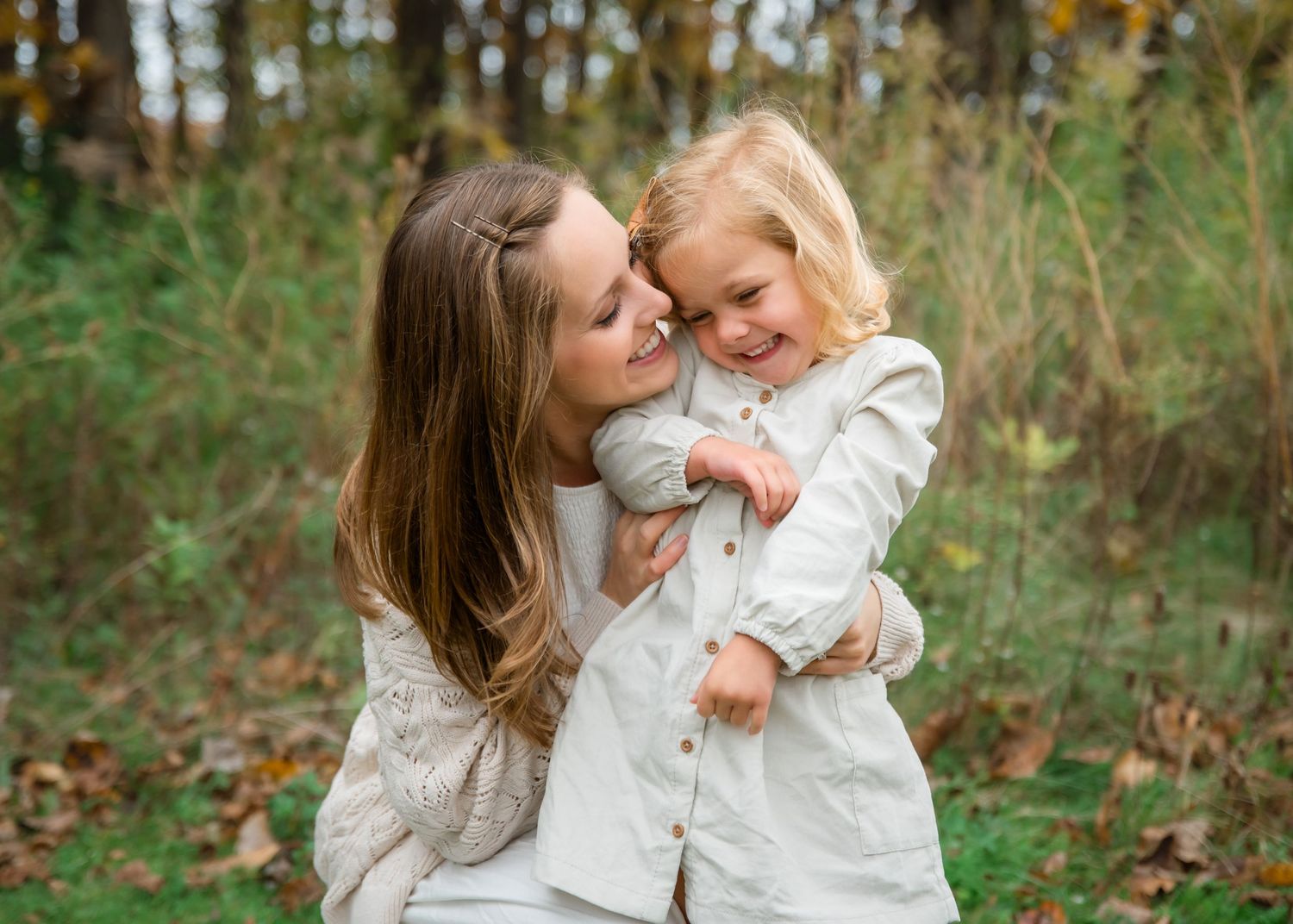 A tender outdoor moment between parent and child wearing matching cream sweaters amid autumn foliage.