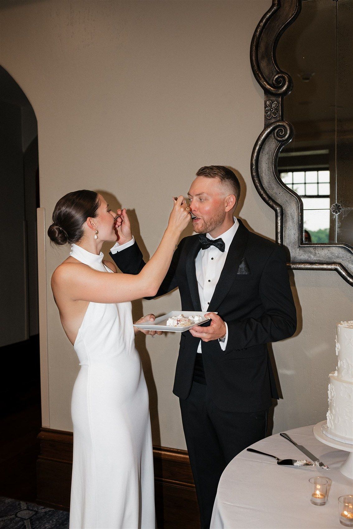 A bride and groom playfully feed each other wedding cake during their reception celebration.