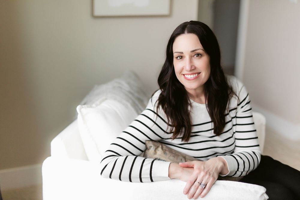 Woman in striped long sleeve shirt relaxing on white couch in bright room with natural light.