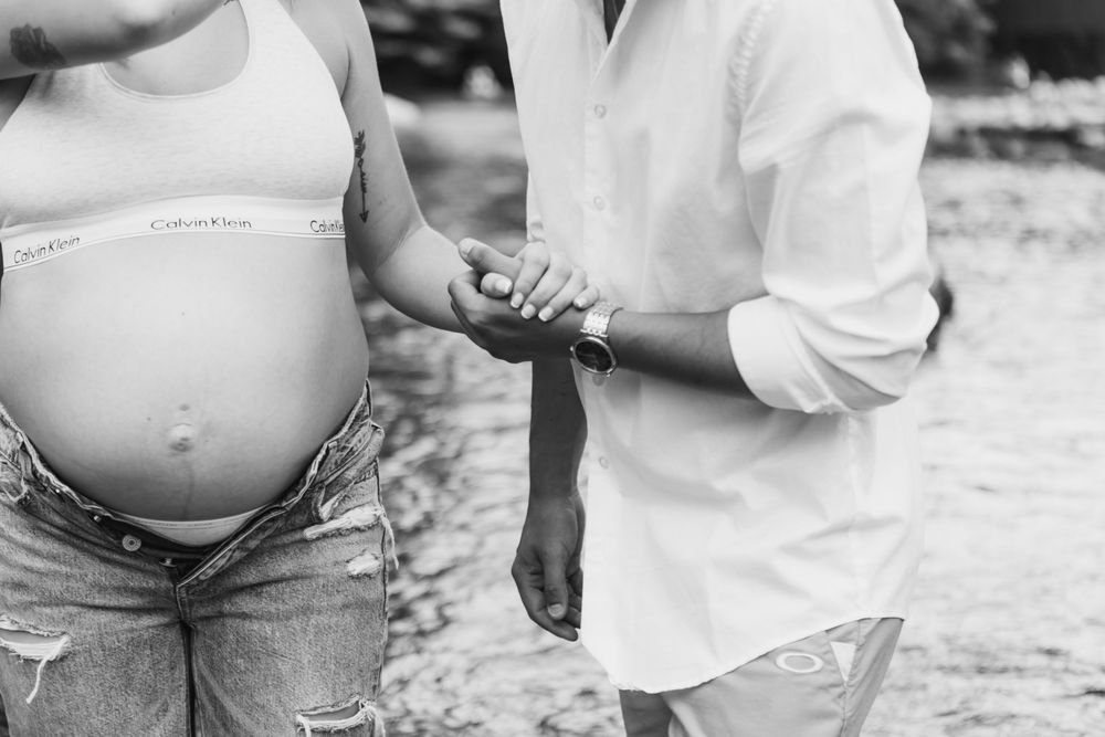 Close up black and white photo of a pregnant belly in denim shorts with someone holding their hand.