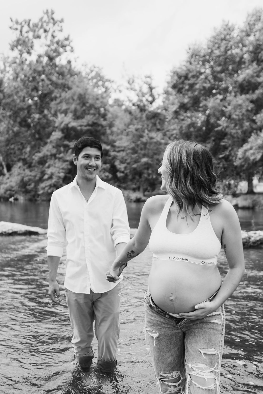 Black and white photos of an expectant couple wading in water during a maternity photoshoot.