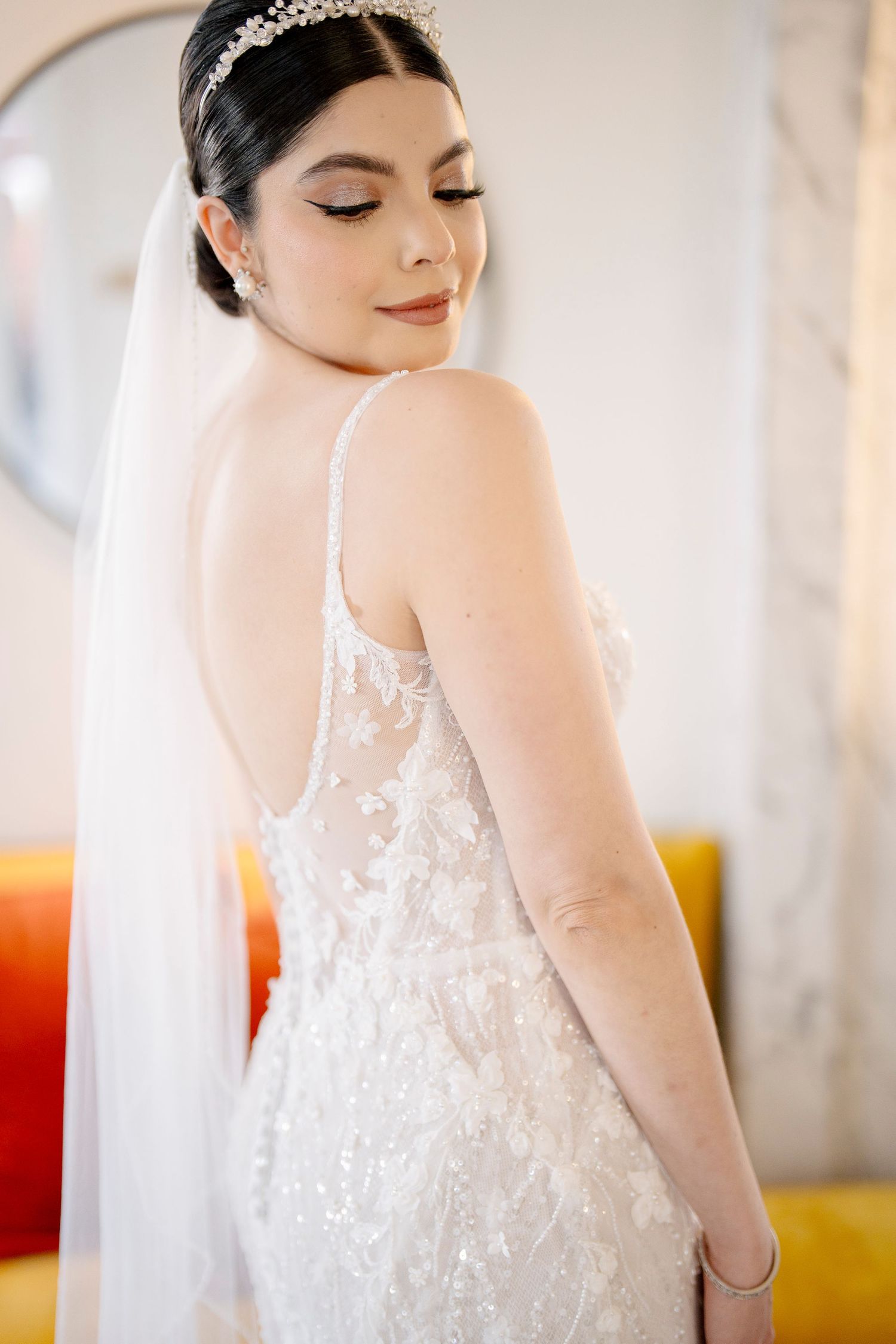 A bride wearing a delicate lace wedding gown with spaghetti straps and veil poses elegantly with eyes closed.