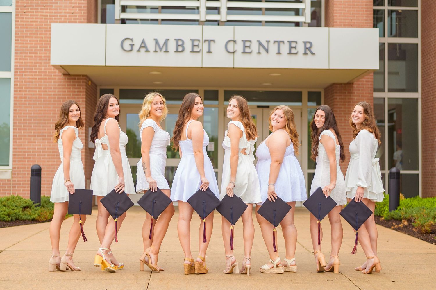 Row of graduates in white dresses posing in front of Gambet Center building.