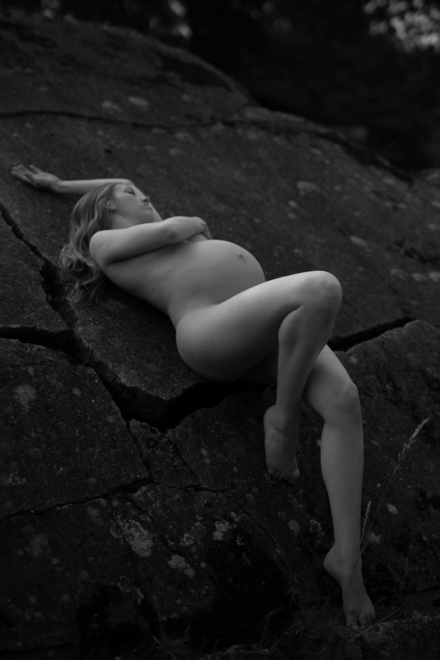 Artistic black and white nude figure reclining on dark rocky terrain, creating a dramatic contrast in light and shadow.