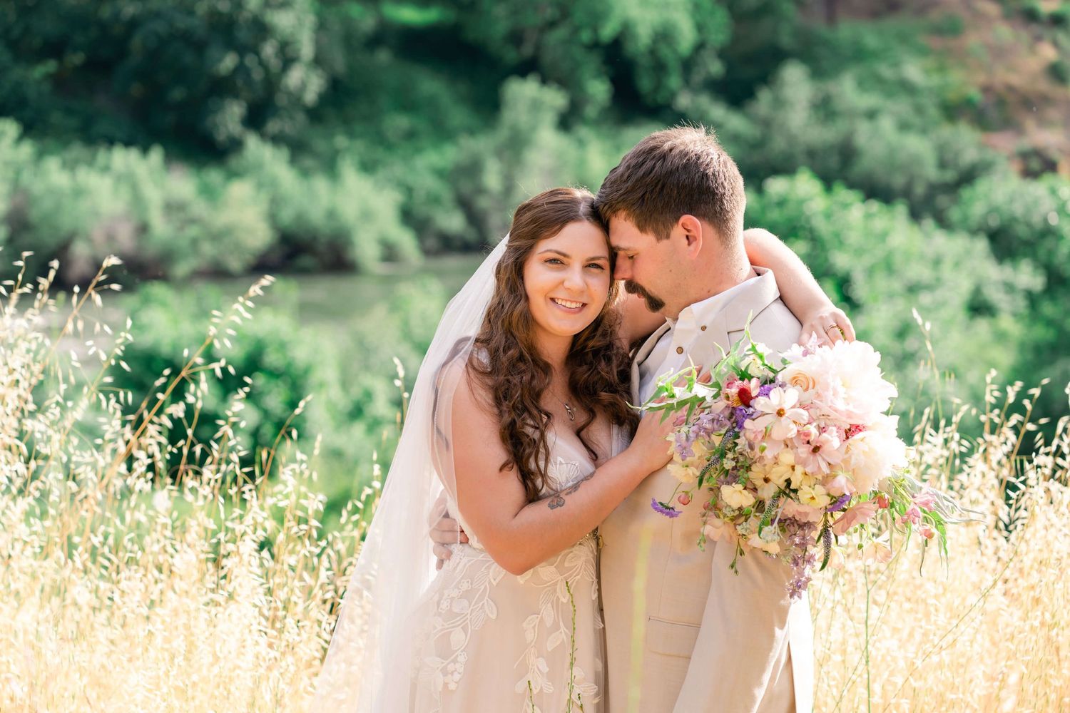 Groom nuzzles into the bride for a wedding portrait with beautiful wildflower bouquet with soft pinks and purples