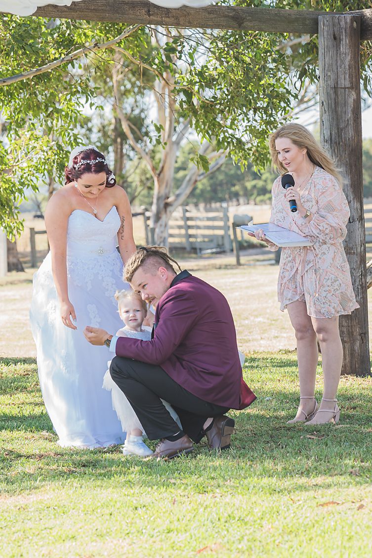 Sweet outdoor wedding ceremony moment captured on a sunny day under a tree at a rustic countryside venue.