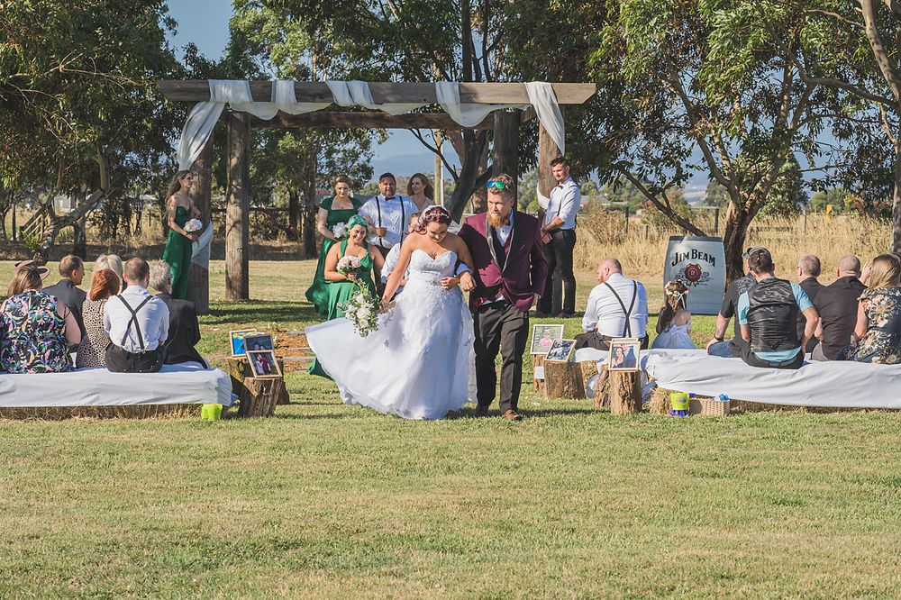 Outdoor wedding ceremony under a wooden arch on a grassy lawn with guests seated on white chairs at sunset.