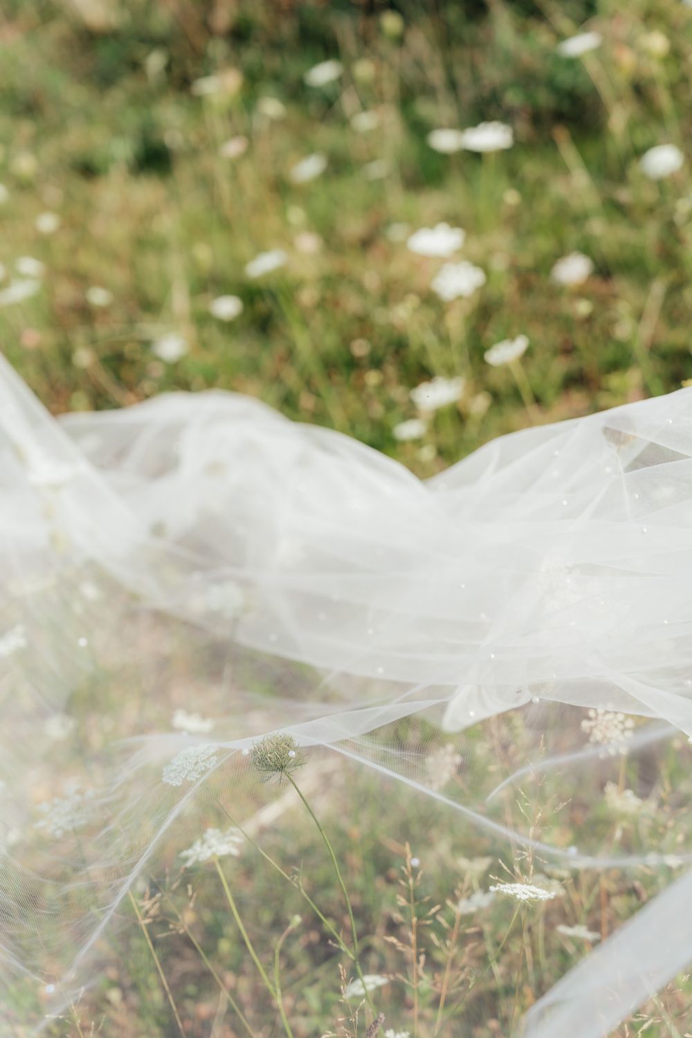 Delicate white tulle veil floating gently over a meadow of wildflowers on a sunny day.
