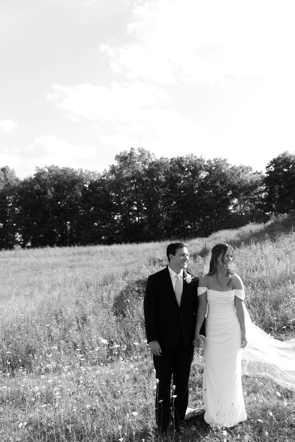 A romantic black and white photo of a bride and groom standing together in a wildflower field.