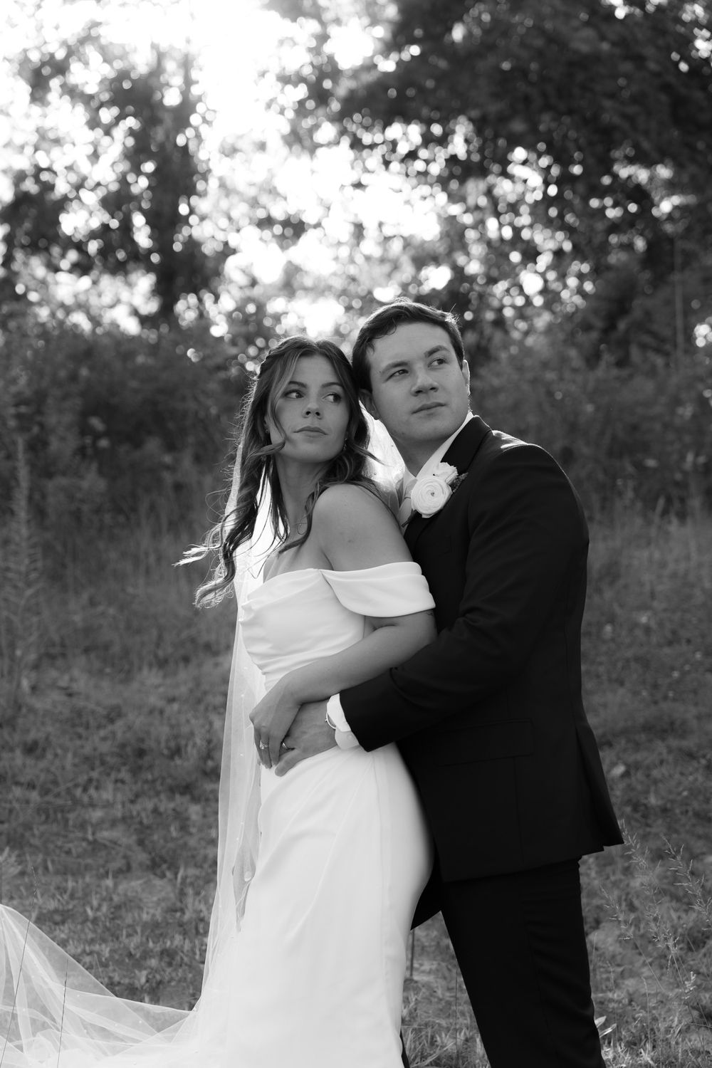 A romantic black and white wedding portrait of a couple posing together in an outdoor setting with trees in the background.