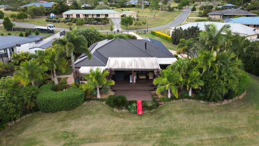 An aerial photograph of a residential property surrounded by lush tropical landscaping, showcasing a gazebo-style roof and a neatly maintain