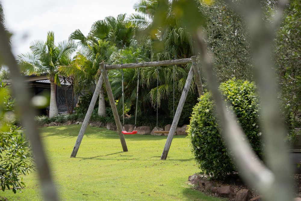 A view of a backyard with a swing set framed by palm trees and hedges, offering a glimpse of a family-friendly outdoor space.