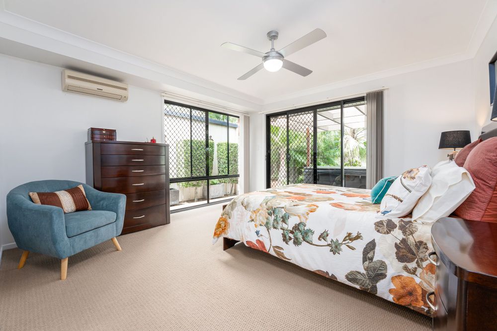 A bright and airy bedroom with large windows, modern furnishings, and a floral bedspread, creating a cozy and inviting atmosphere.