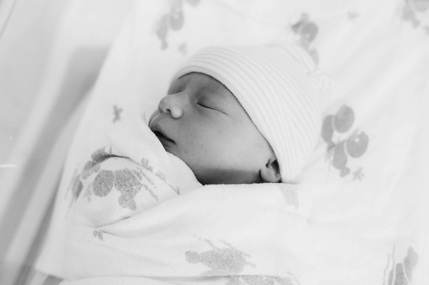 A peaceful sleeping newborn baby wearing a white hat rests among soft floral blankets in black and white.