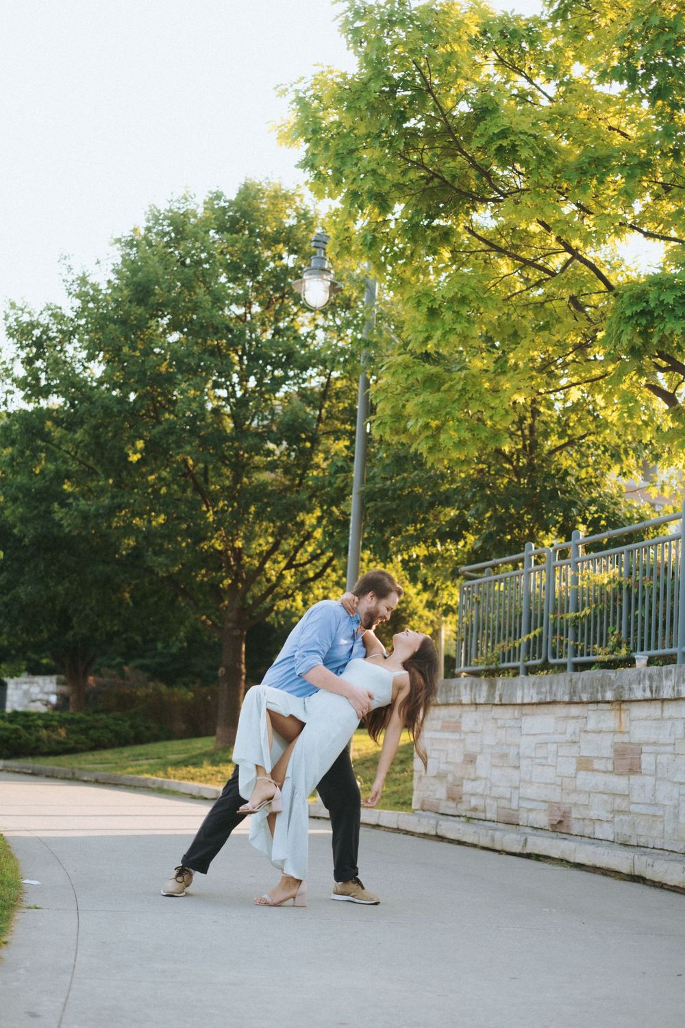 A romantic dance move performed on a curved pathway near trees and stone wall.