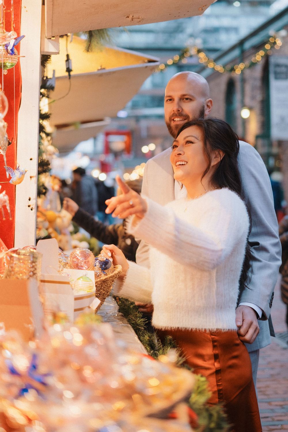 Couple sharing intimate moments at a festively decorated outdoor market with string lights.