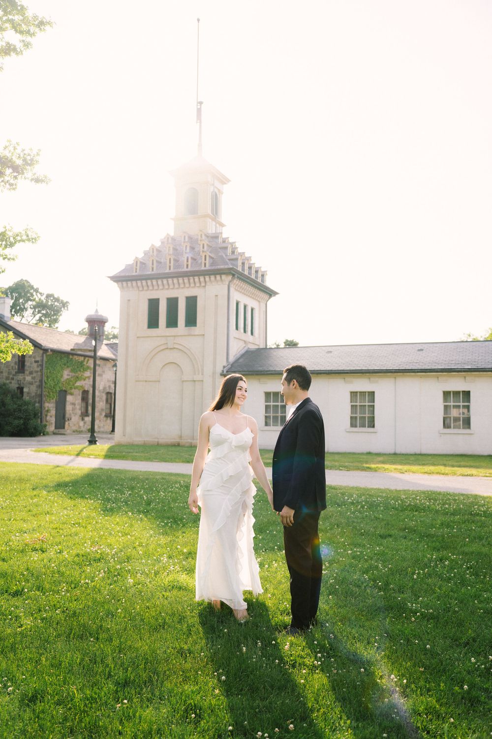Newlywed couple walks hand in hand across a grassy lawn beside a white church building on a sunny spring day.