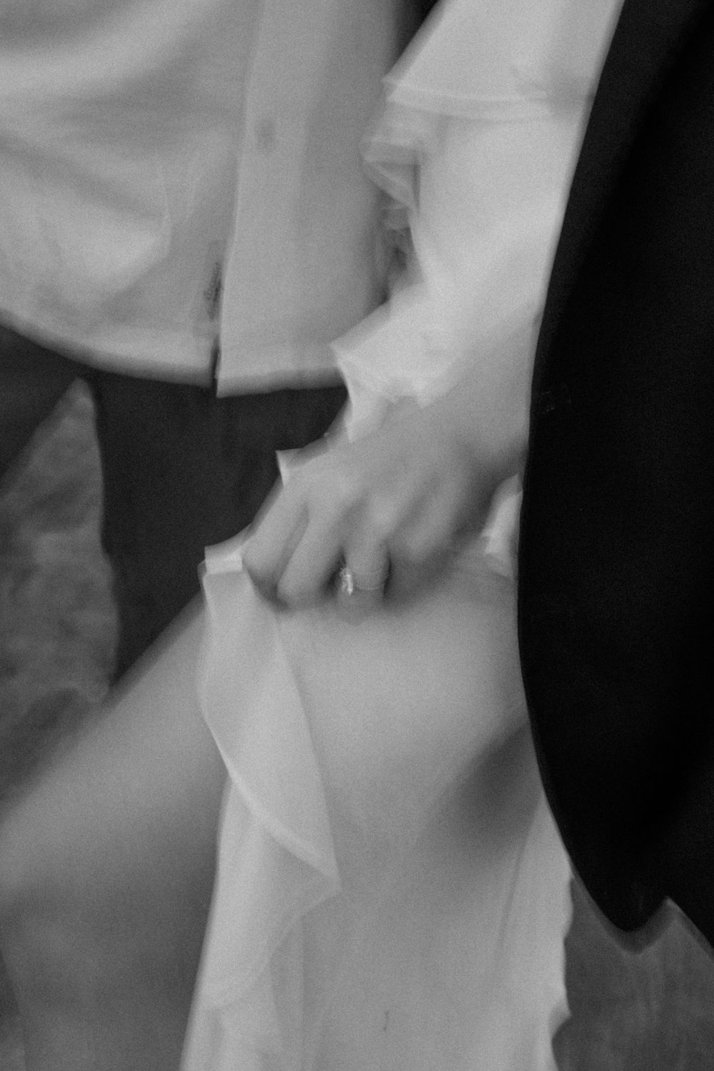 A black and white close-up of a couple holding hands, with the bride wearing a flowing white wedding dress.