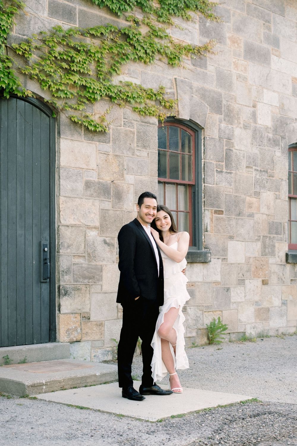 A couple in formal attire share romantic moments against a stone wall with climbing ivy at different angles.