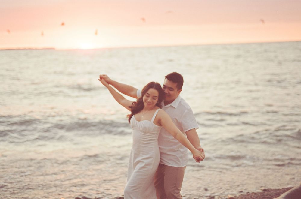 A romantic beach photoshoot at sunset with soft pink skies and waves.