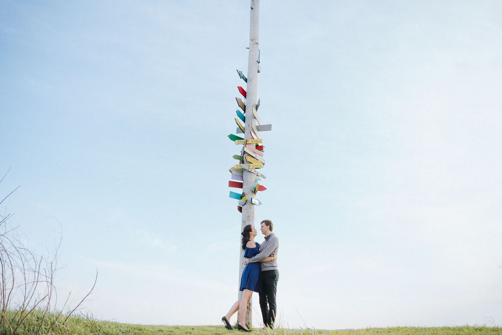 A couple embraces near a pole decorated with colorful flags against a blue sky.