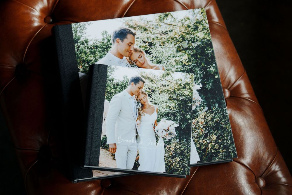 A wedding photo album lying on a brown leather couch shows a bright outdoor ceremony scene.