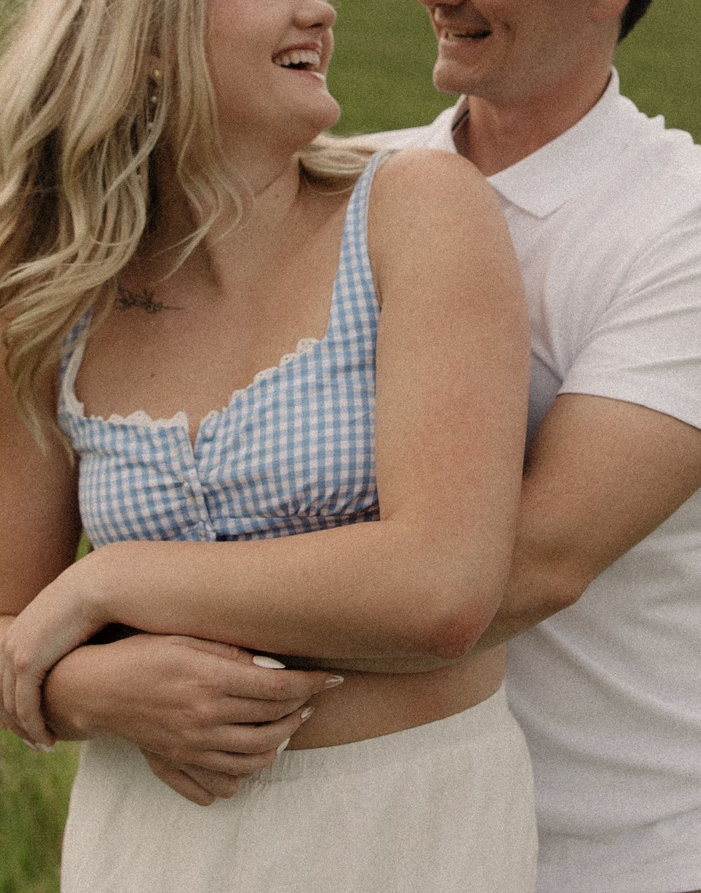 Close-up view of a couple embracing, wearing a blue gingham dress and white shirt in a romantic outdoor setting.