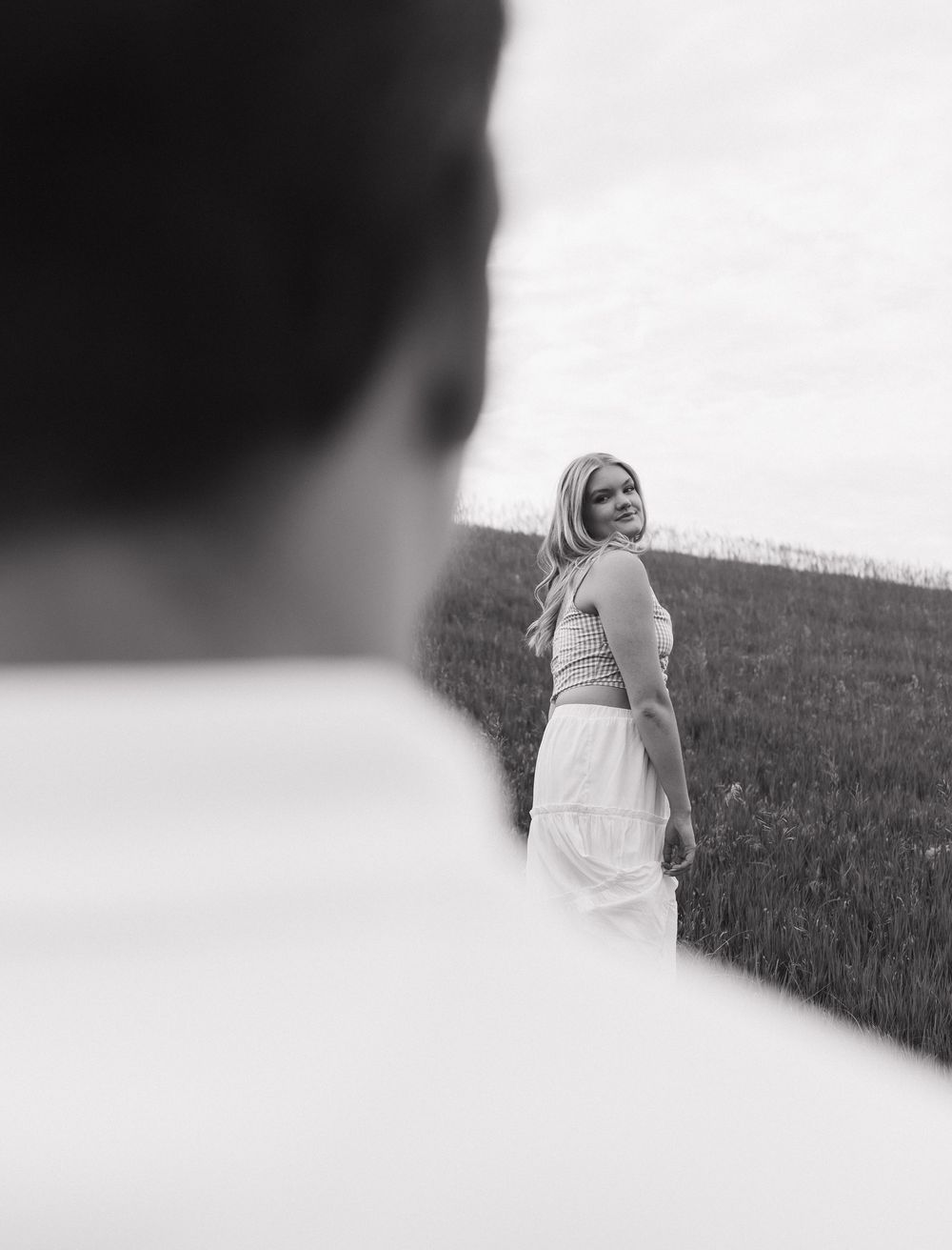 A dreamy black and white photo taken from behind showing a person in a white dress standing on a grassy hillside.