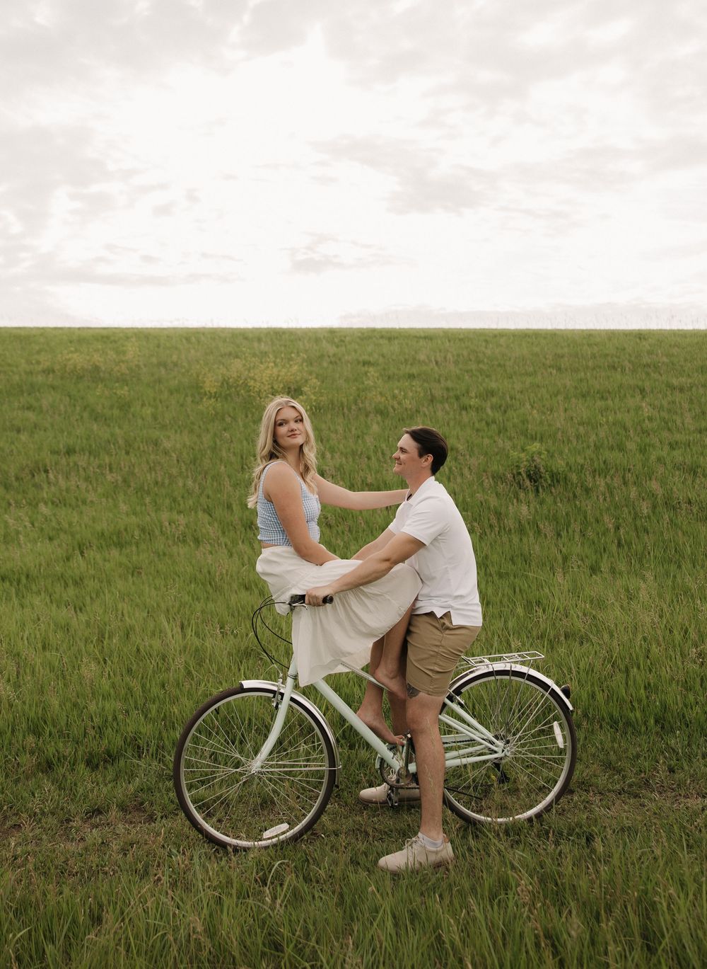 Two figures share a playful moment on a vintage white bicycle in a green meadow during a warm afternoon.