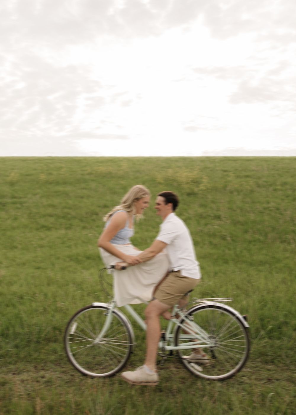 A romantic scene in a meadow with a couple sharing a moment on a vintage white bicycle.