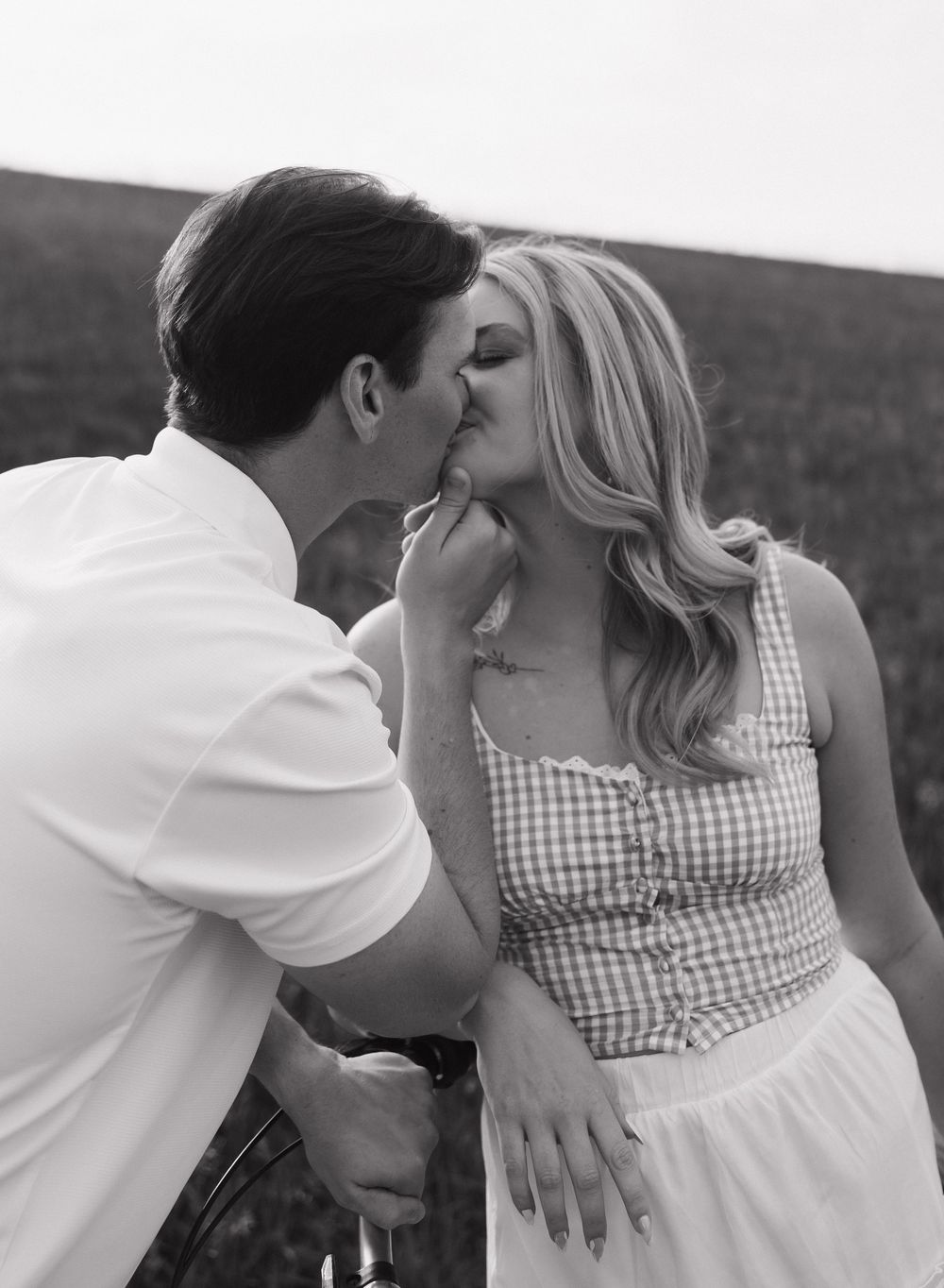 A romantic black and white portrait of a couple sharing an intimate moment in a meadow.