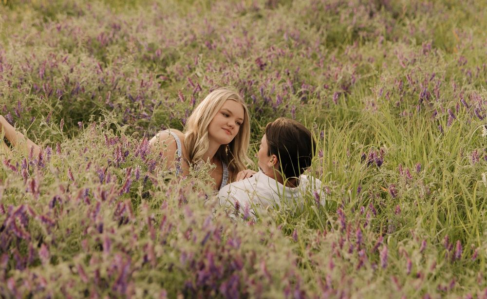 Two people share an intimate moment while laying in a field of purple wildflowers.