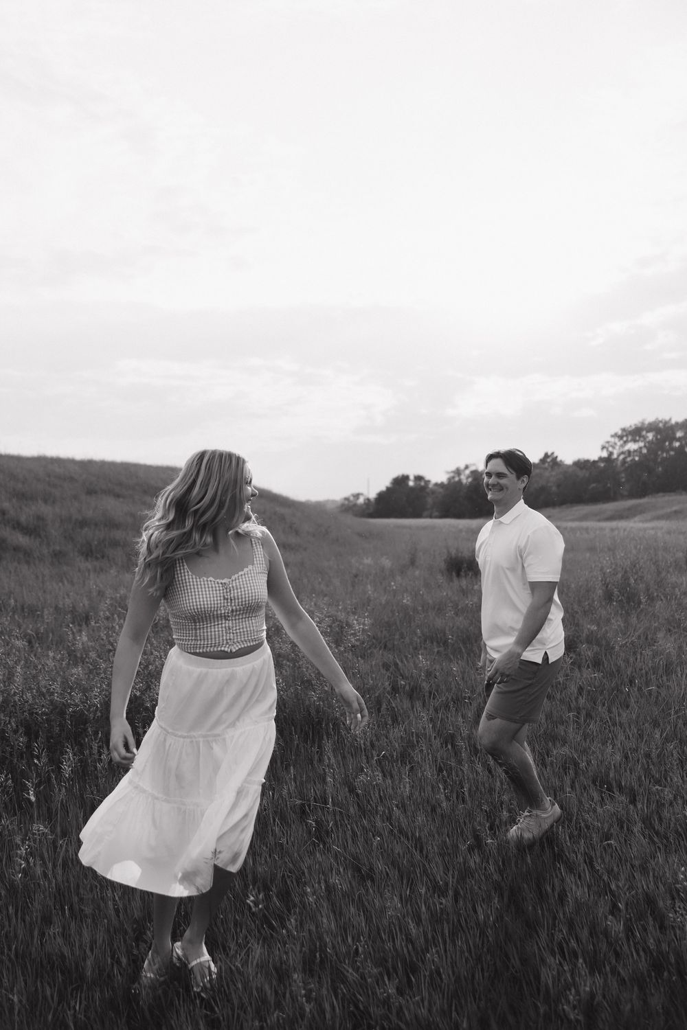 Playful couple running through a grassy hillside at sunset in black and white.
