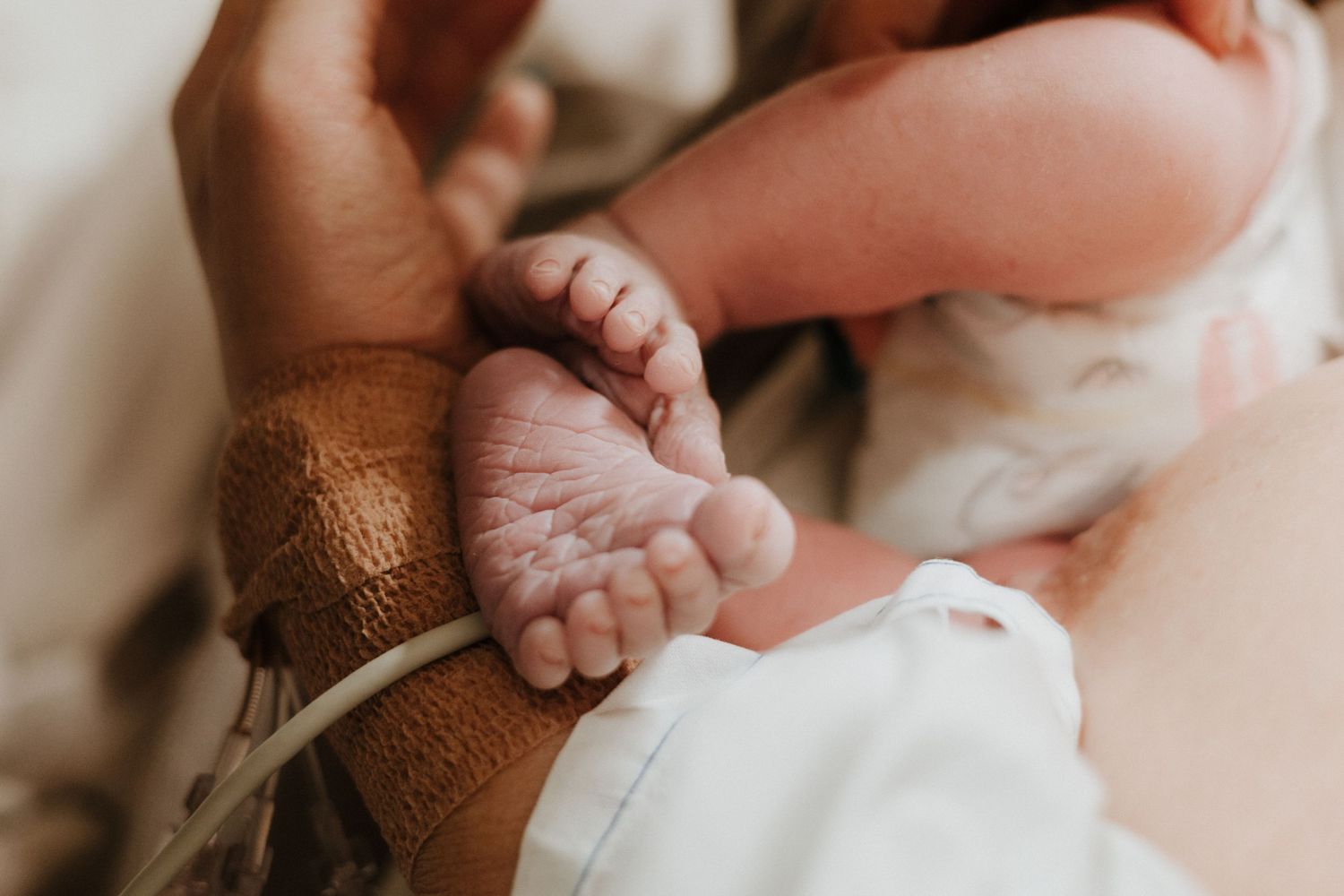 Close-up view of tiny newborn baby feet resting on white bedding with gentle hands touching.