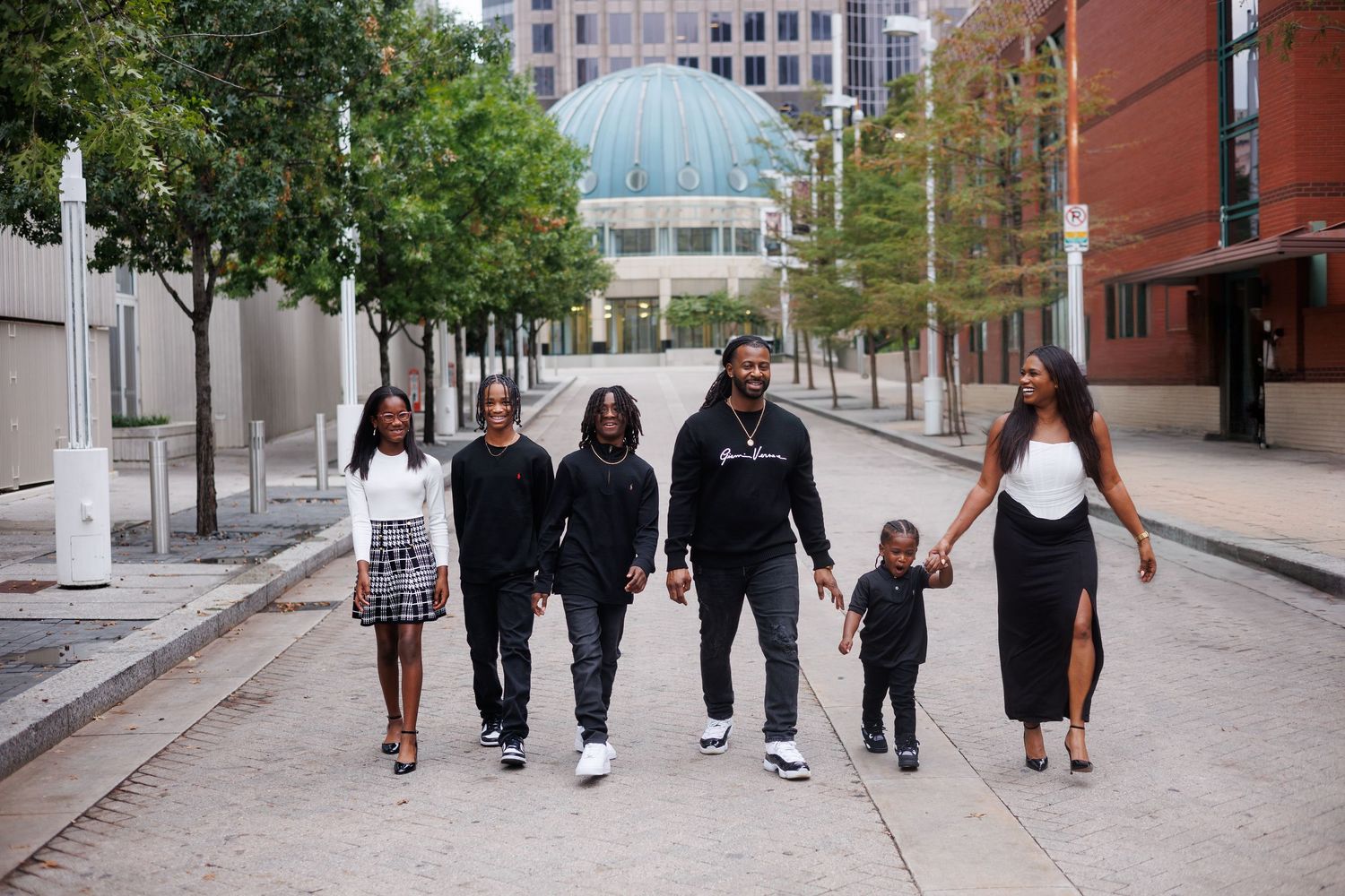 Family dressed in coordinating black and white outfits walks on a Dallas city street for family portraits