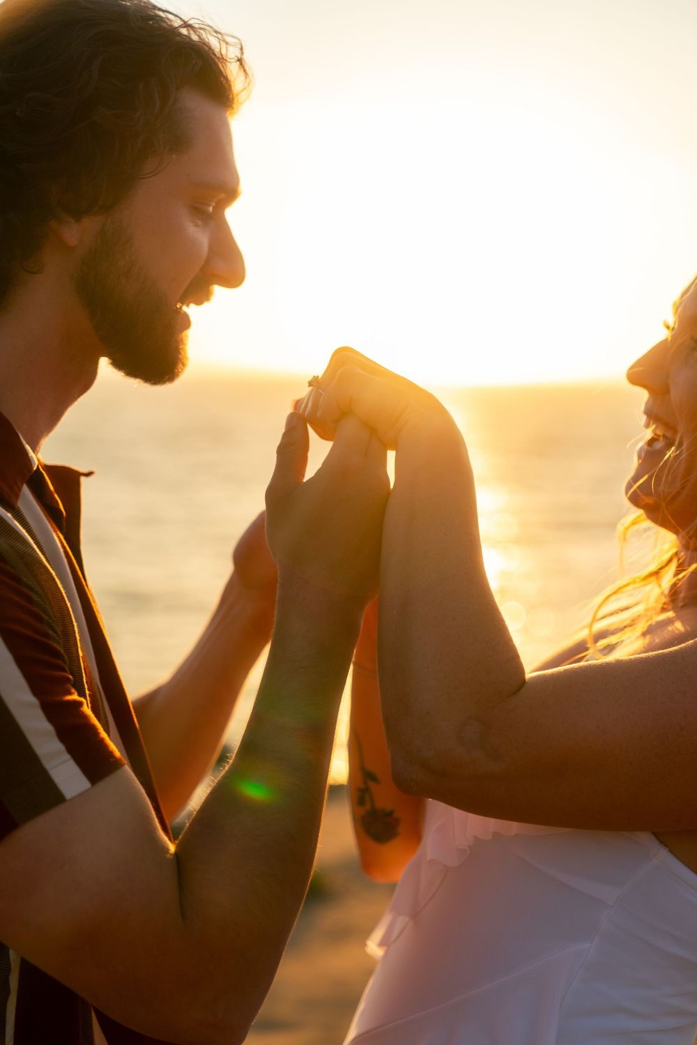 A couple sharing a romantic moment at sunset by the ocean silhouetted against golden light.