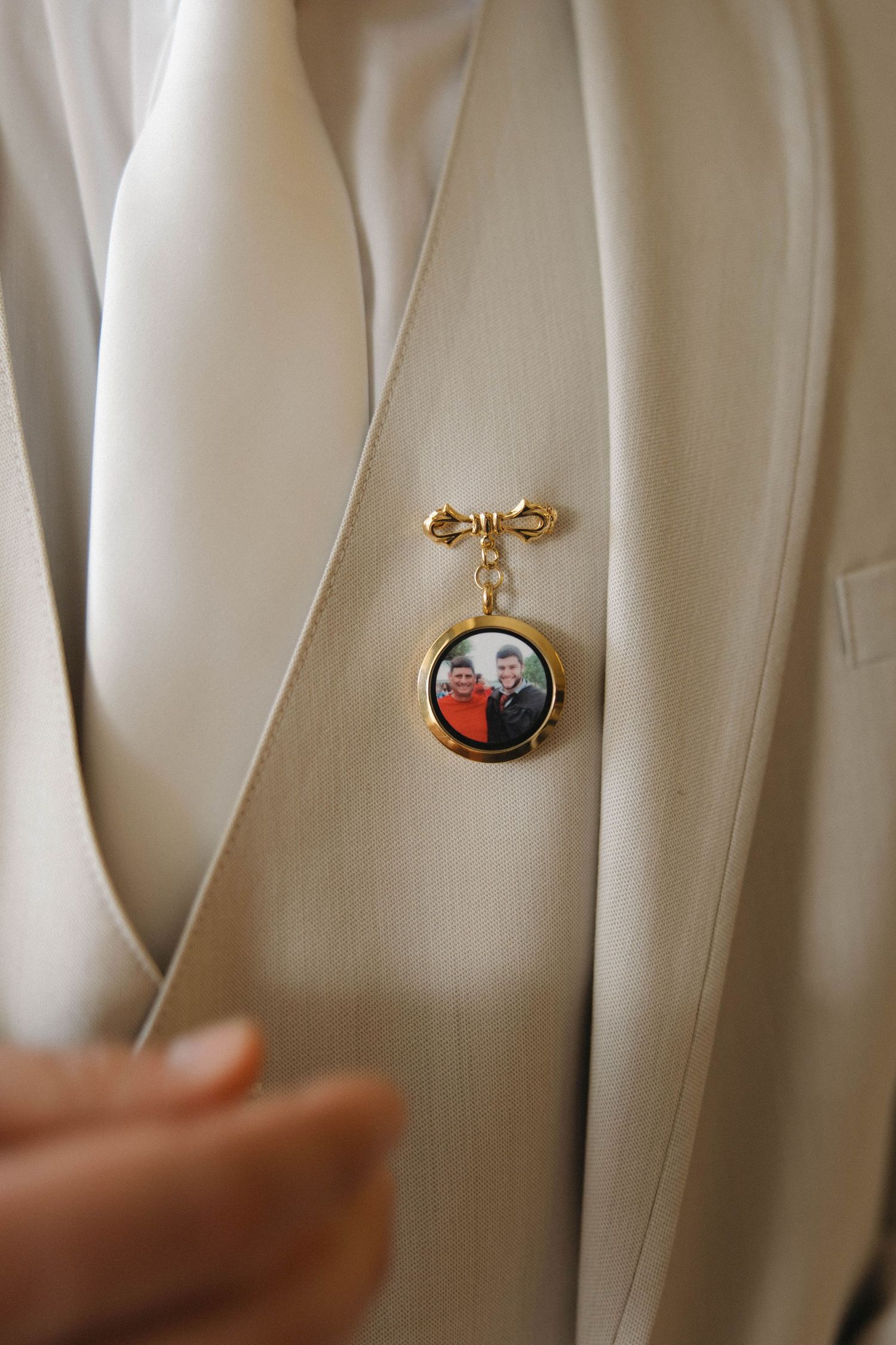 A person in a white suit adjusts their tie while looking in a mirror near a window.